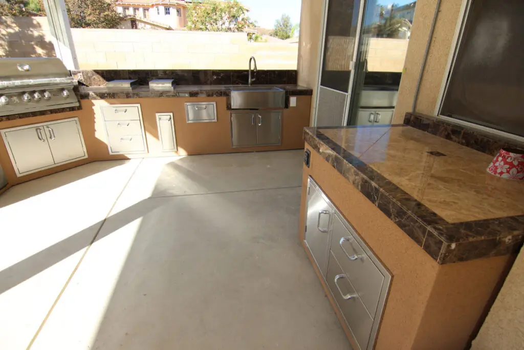 Full view of a custom outdoor kitchen island layout in Orange County with built-in grill, sink, drawers, and marble countertops under a covered patio