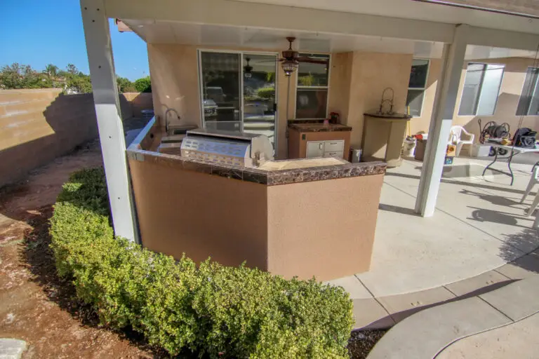 Compact outdoor kitchen under covered patio with marble countertops, built-in grill, sink, and storage in an Orange County backyard