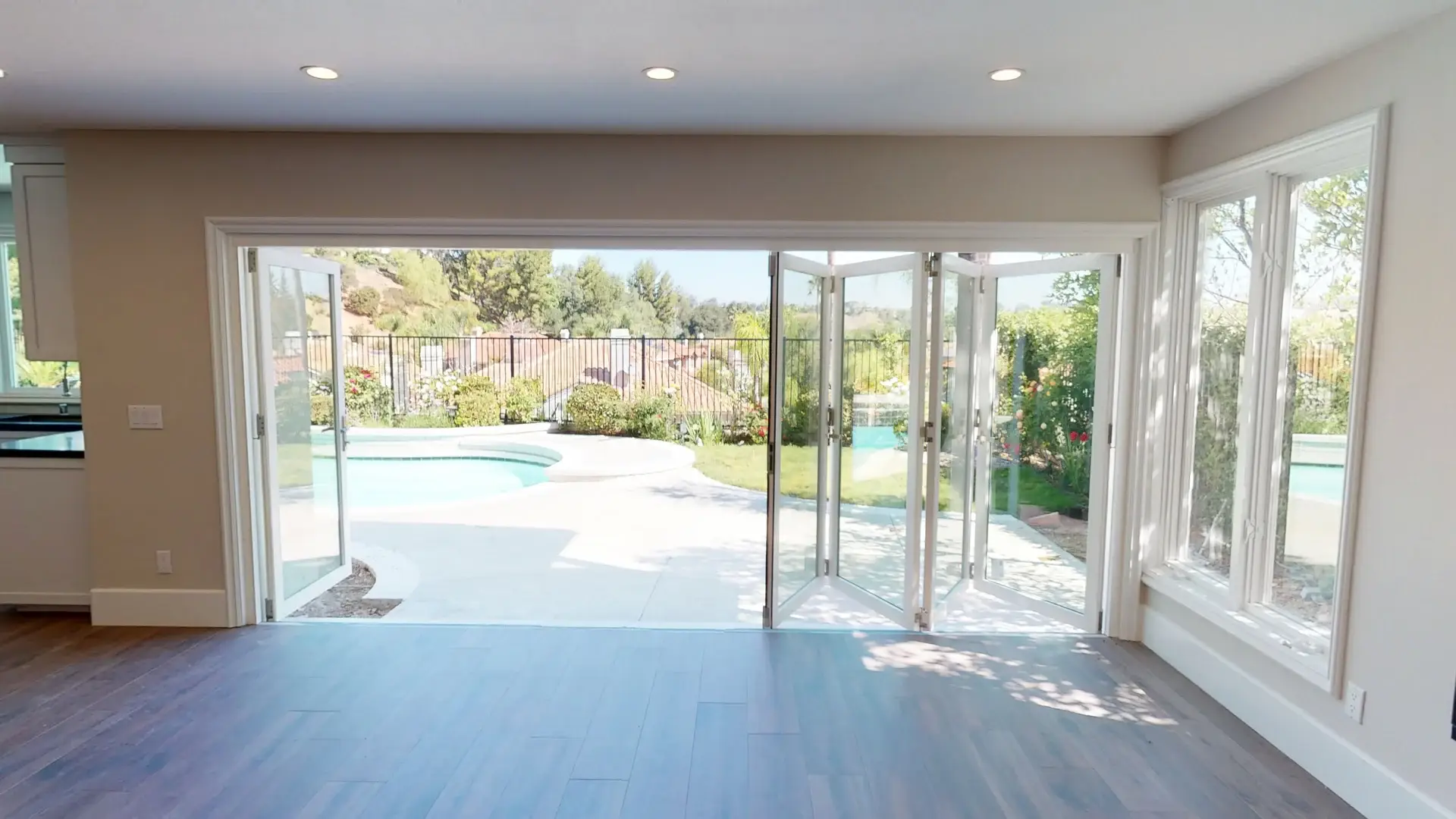 Spacious living room with wide folding glass patio doors fully open to reveal a backyard pool and garden, creating seamless indoor-outdoor flow.