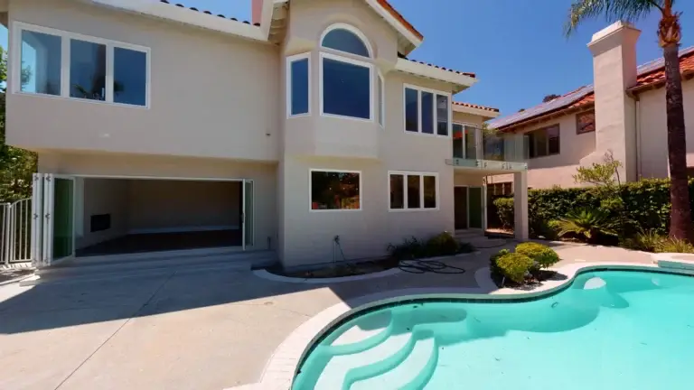 Fully remodeled backyard showcasing a poolside view of a modern two-story home with large glass doors and windows, part of a comprehensive whole house makeover project.