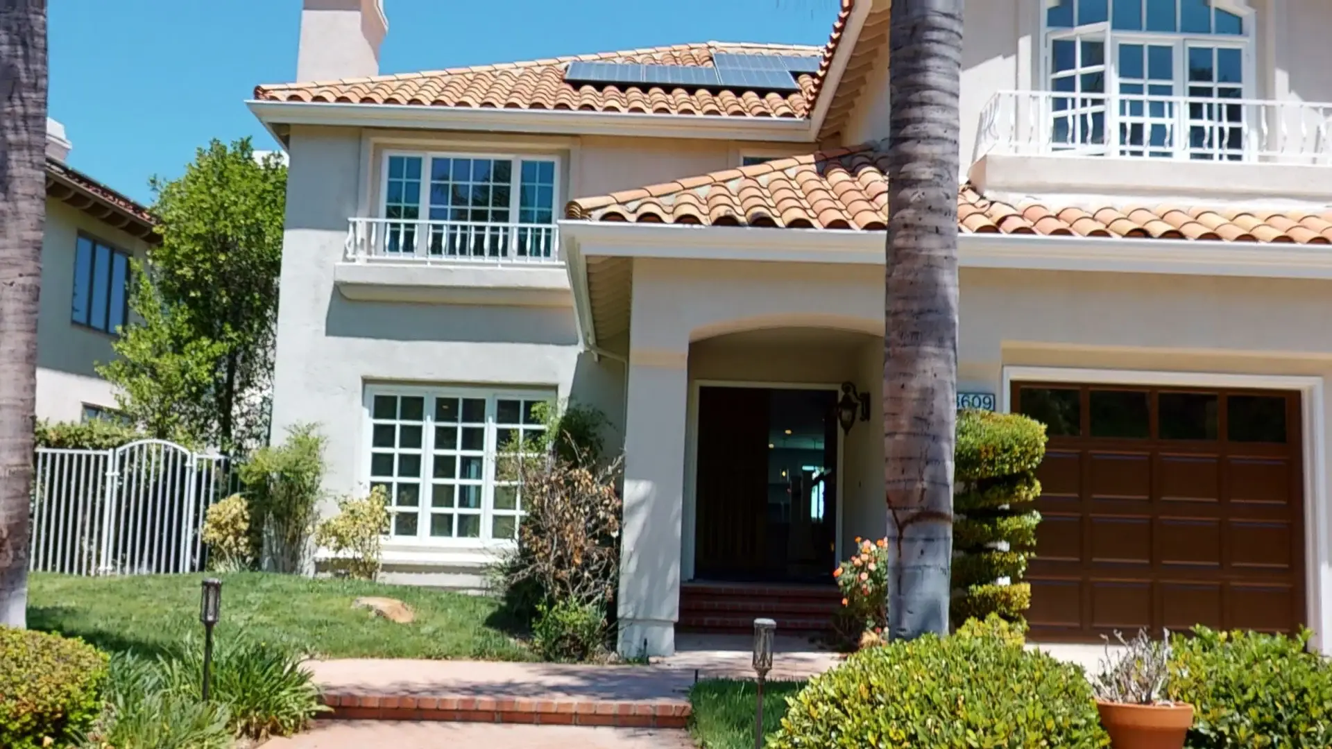 Front view of a remodeled Mediterranean-style house with terracotta roof tiles, white balcony railings, and updated landscaping as part of a whole house makeover project.