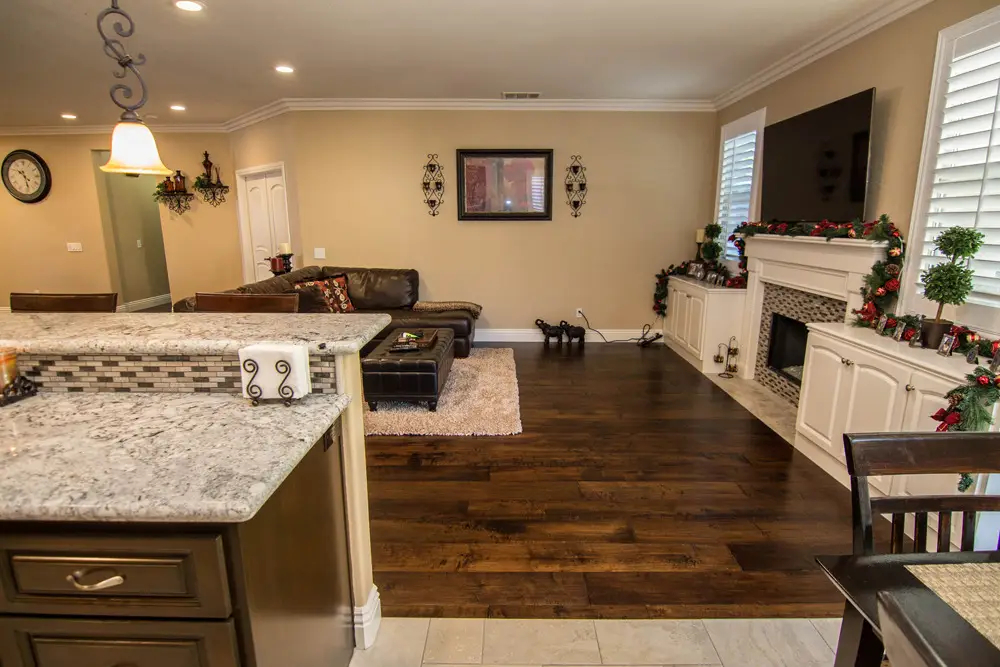 Open concept living room and kitchen with granite countertops, dark wood floors, and a cozy fireplace decorated for the holidays.