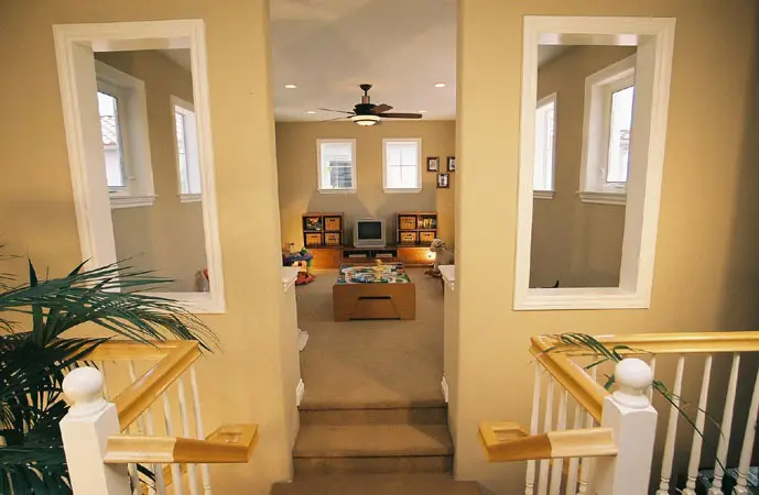 Spacious kids’ playroom room addition located upstairs, featuring custom white stair railing, dual wall openings, and ample windows for natural lighting and ventilation.
