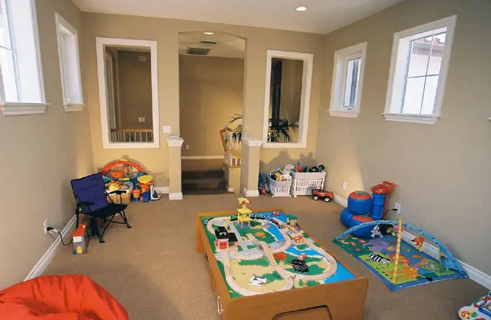 Spacious kids’ playroom room addition featuring a central train table, toy storage bins, colorful play mats, and multiple windows for natural light with built-in wall niches for open visibility.