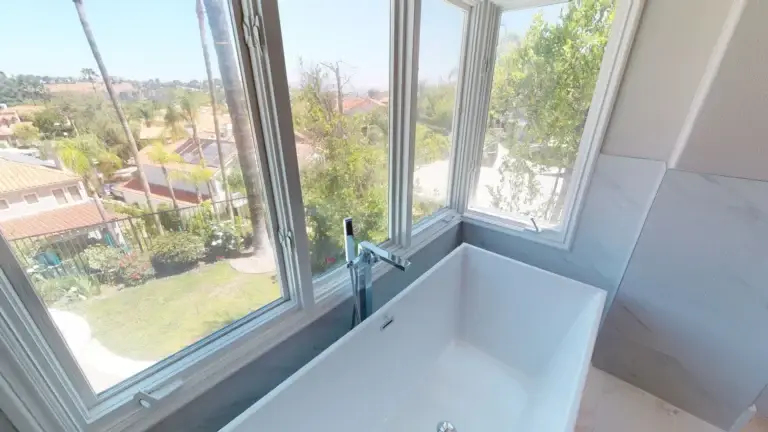 Luxurious soaking bathtub positioned by panoramic corner windows offering serene outdoor views, part of a modern whole house makeover.