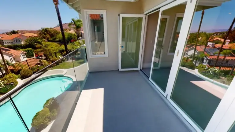 Modern second-floor balcony with sleek glass railing and poolside view, part of a whole house makeover featuring outdoor access and upgraded finishes in Southern California.