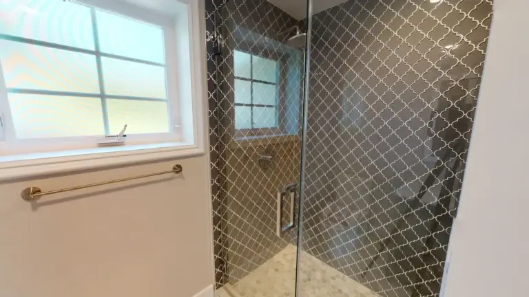 Frameless glass shower with patterned tile wall and brass towel bar, completed as part of a full bathroom transformation during a whole house makeover in Orange County.
