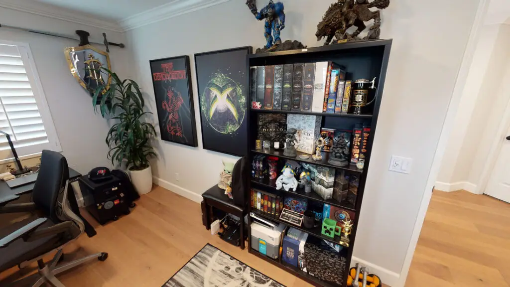 Room addition transformed into a gaming and collectibles space, featuring a black bookshelf filled with action figures, game memorabilia, and art prints.