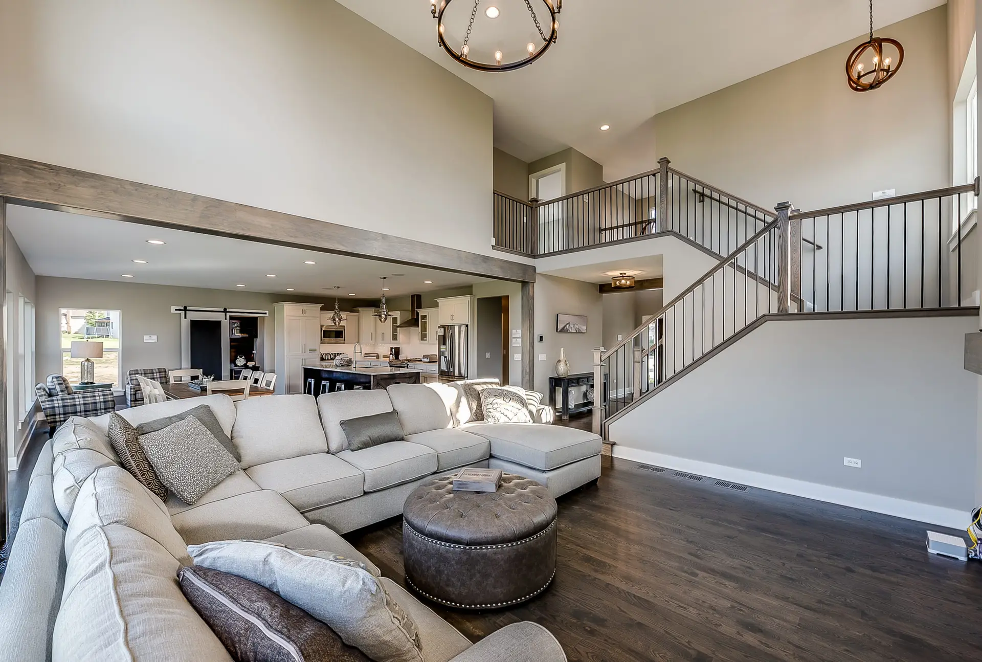 Open-concept room addition featuring a large sectional, modern kitchen, dark wood floors, and a second-story loft with custom stair railing and vaulted ceilings.
