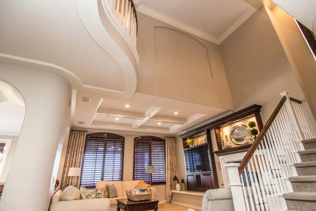 Sophisticated room addition featuring a grand two-story ceiling, curved interior balcony, detailed molding, and custom built-in shelving that enhances both space and style.