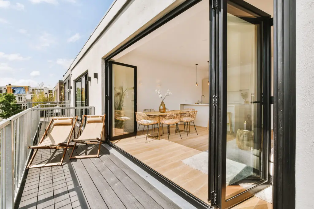 Stylish room addition featuring bi-fold glass doors opening to a spacious balcony with lounge chairs, connecting indoor dining to outdoor living seamlessly.