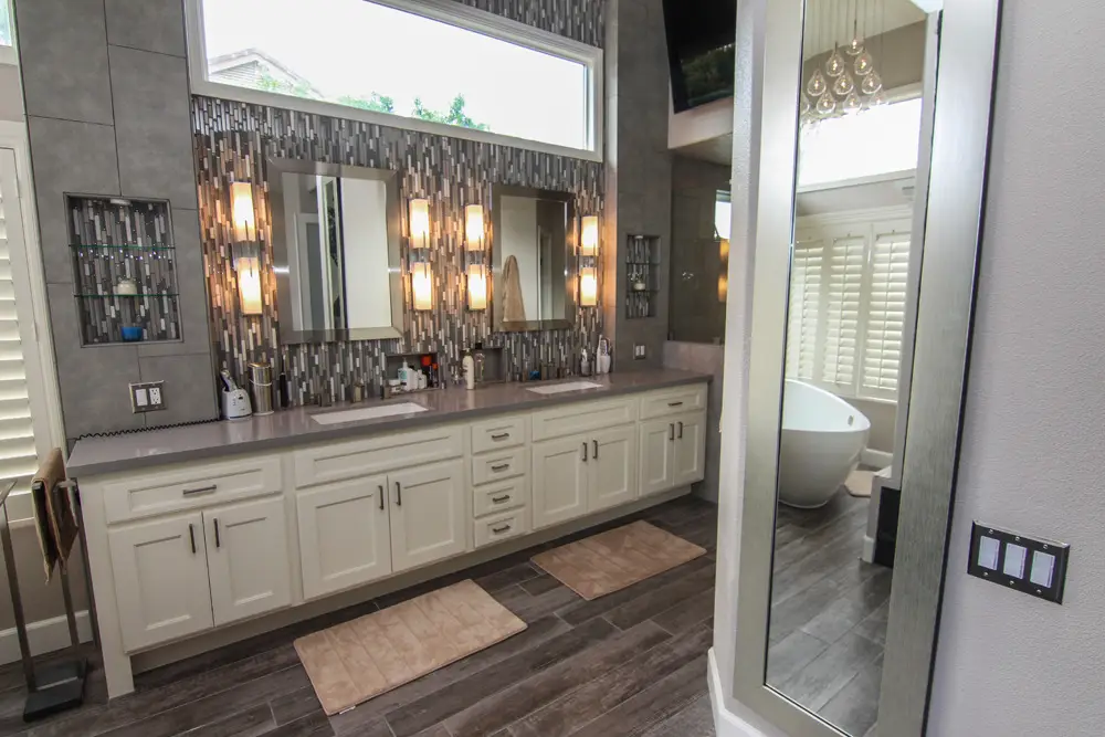 Contemporary bathroom remodel featuring a long double vanity with white shaker cabinets, mosaic tile backsplash, and vertical light sconces for a sleek, spa-like design