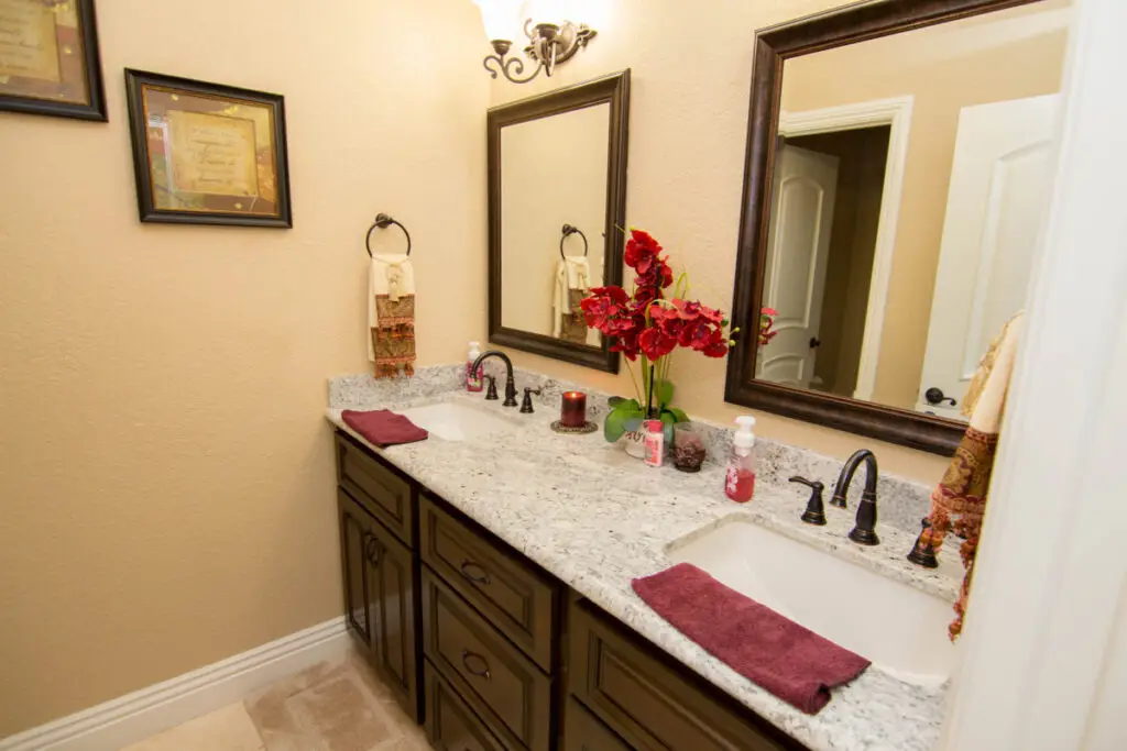 Classic bathroom renovation featuring a double sink vanity with granite countertops, oil-rubbed bronze faucets, framed mirrors, and decorative red accents
