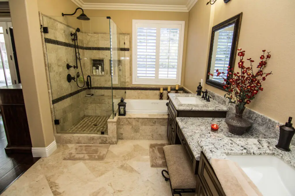 Upscale bathroom renovation featuring a walk-in frameless glass shower, marble tile floors, granite countertops, dual vanity, and a soaking tub with plantation shutters.