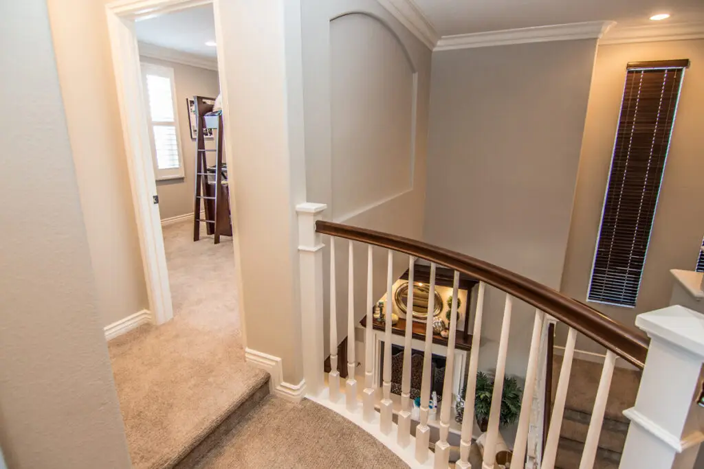 Beautiful upstairs room addition featuring plush carpeting and a smooth hallway transition into a new bedroom, highlighted by elegant crown molding and custom railing work.