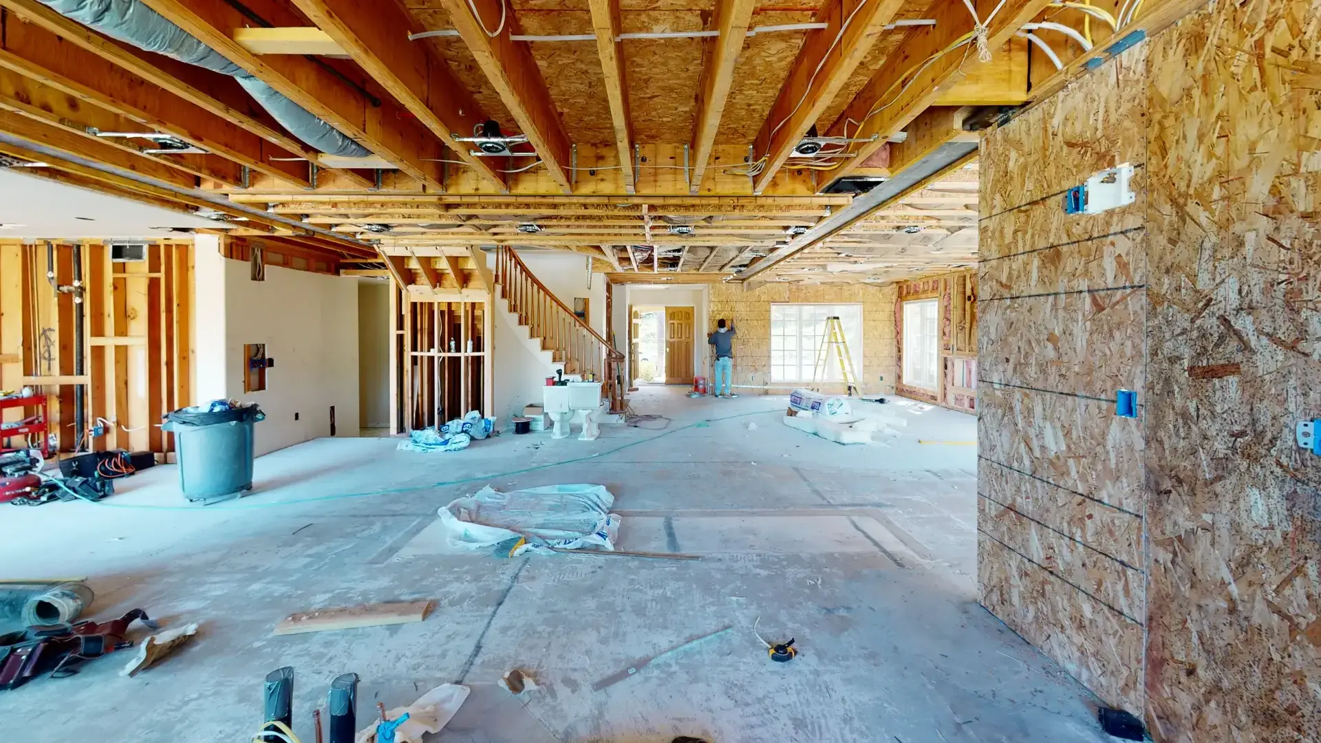 Ongoing whole house makeover project showing exposed ceiling framing, rough plumbing, electrical, and HVAC installations with open layout and visible construction tools.