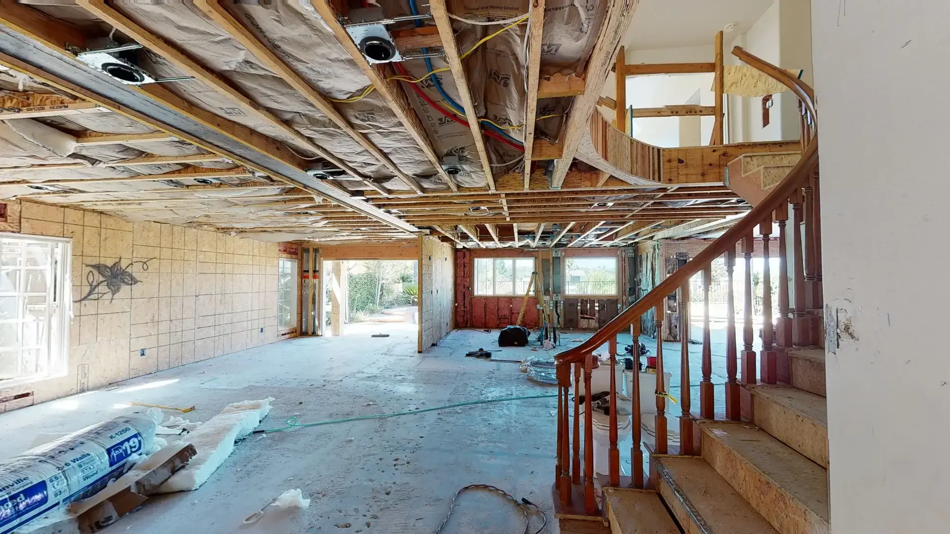 Full home makeover project showing open framing, ceiling insulation, exposed utilities, and a custom curved staircase structure in progress.