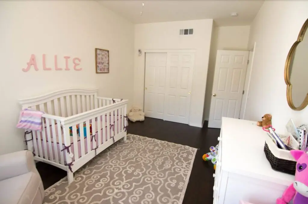 Finished garage conversion showcasing a bright nursery room with custom closet doors, hardwood flooring, and white baby crib setup
