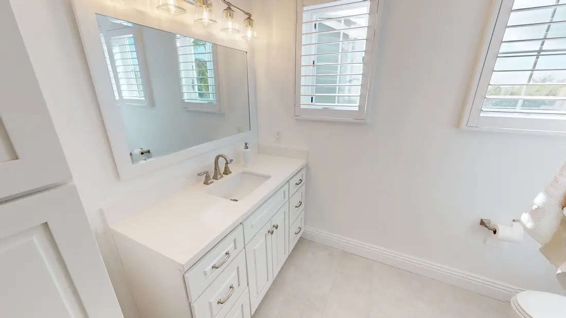 Elegant white bathroom vanity with quartz countertop, brushed nickel fixtures, large mirror, and natural light from shuttered windows