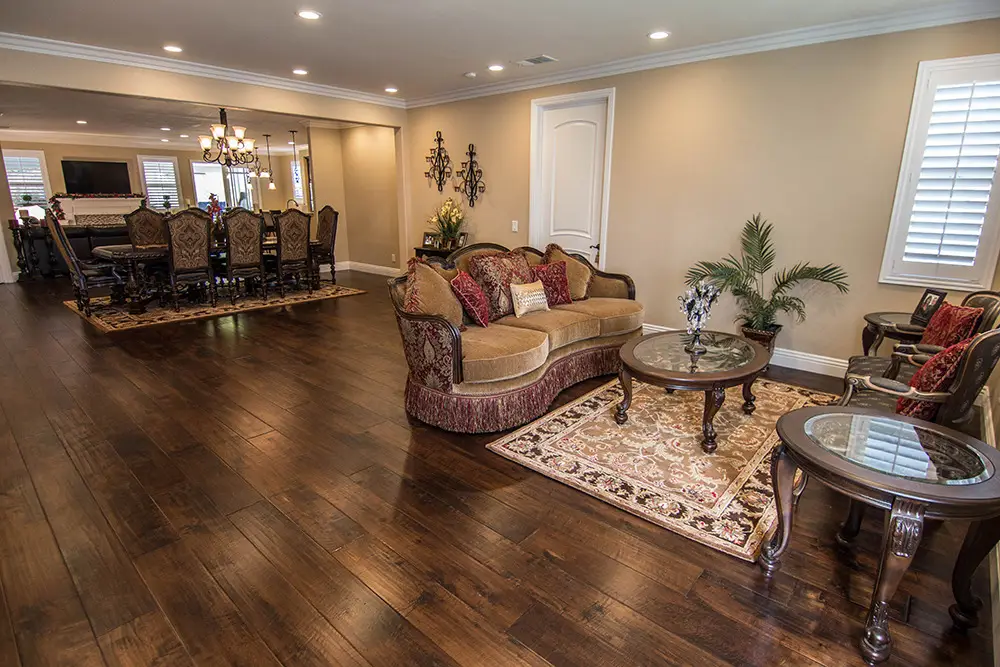 Spacious open-concept living and dining area with dark hardwood floors, traditional furniture, recessed lighting, and neutral wall colors, showcasing a full interior home remodel with a cohesive classic design style.