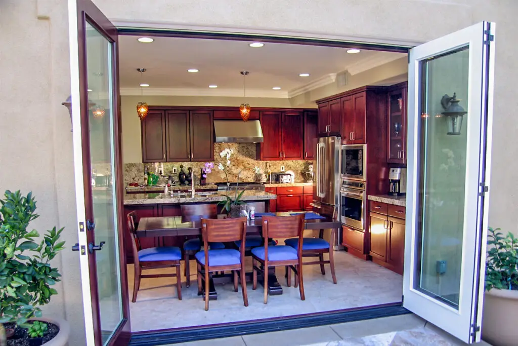 Beautiful kitchen remodel featuring custom dark wood cabinetry, granite countertops, stainless steel appliances, and bi-fold doors that open to a patio for seamless indoor-outdoor living.