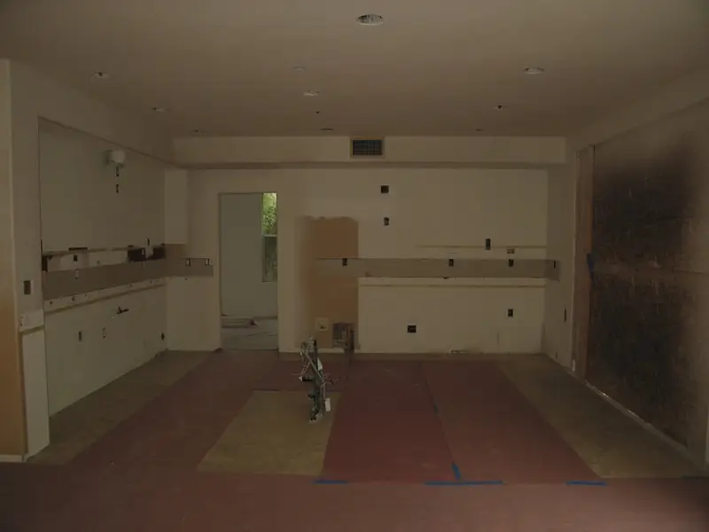 Kitchen remodel in progress showing rough-in plumbing and electrical setup, with protective floor covering and wall preparation.