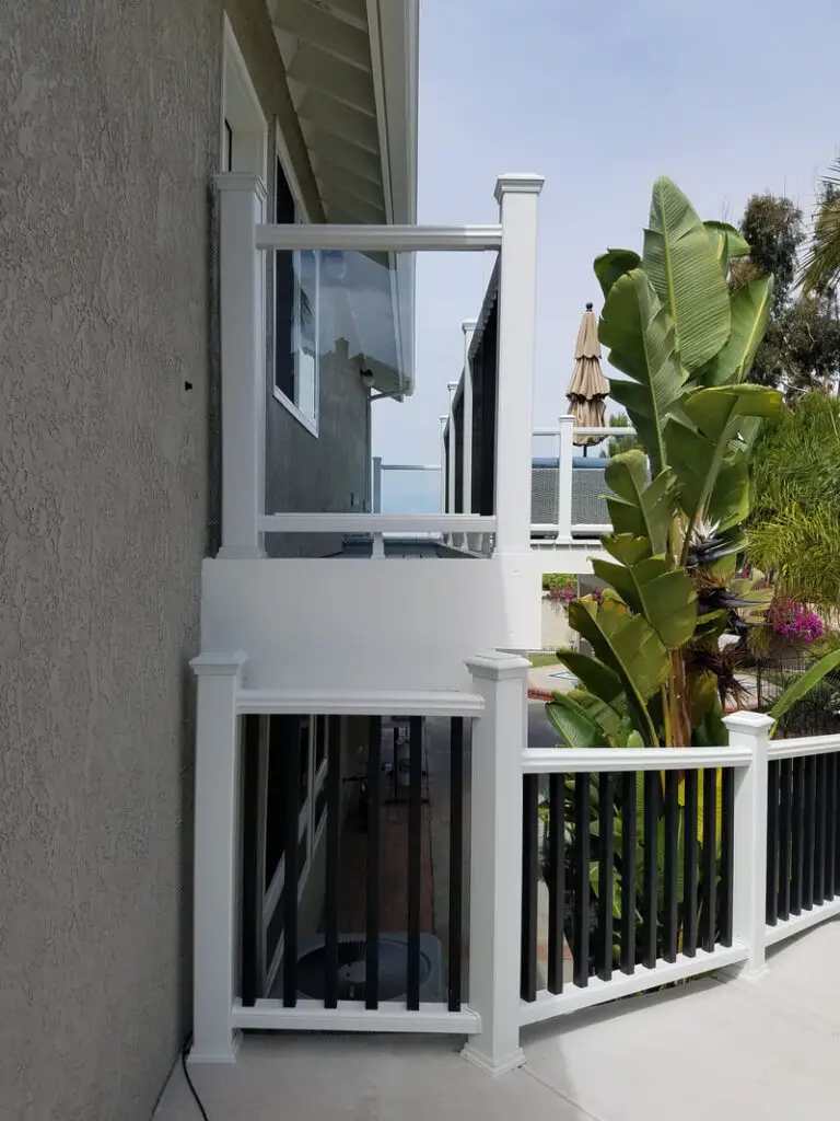 Custom deck with white and black railing, glass panel section, and side stair access beside home in Orange County