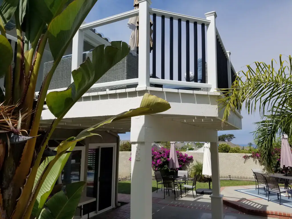 Modern elevated backyard deck with white posts and black railing, built above patio area in Southern California home