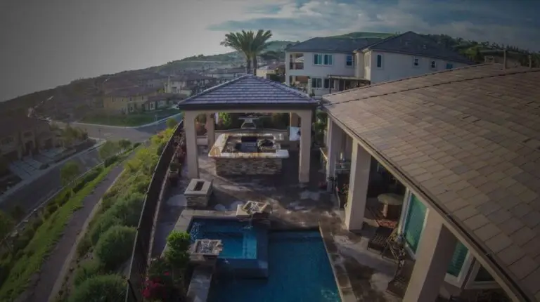 Luxury backyard remodel in Orange County featuring an outdoor kitchen, covered California room, pool, fire pit, and hillside view