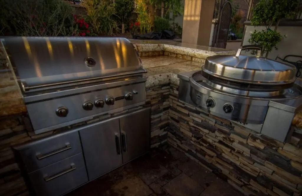 Close-up of a built-in outdoor grill and Evo cooktop with stone veneer and granite countertops in a custom Orange County backyard kitchen