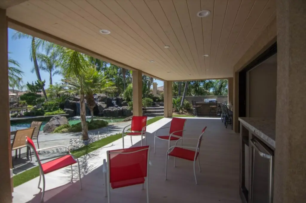 Contemporary California room featuring a wood-paneled ceiling, built-in outdoor bar, and red patio seating overlooking a landscaped backyard in Orange County